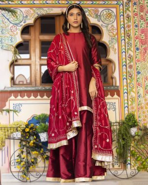 Maroon taffeta silk sharara set with short kurta featuring highlighted back neckline and gota detailing, matching sharara, and silk organza dupatta with aari embroidery and gota accents in Golden Muslin by Priyanka Rathore