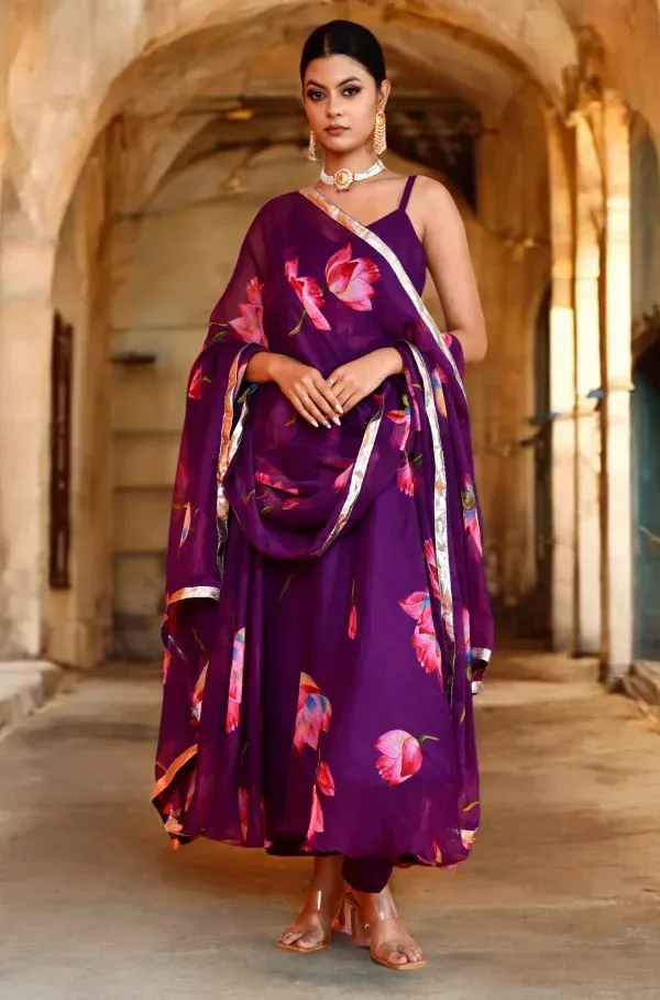 A flowing purple chiffon Anarkali featuring delicate lotus prints and Golden Muslin detailing, designed by Priyanka Rathore for festive elegance.