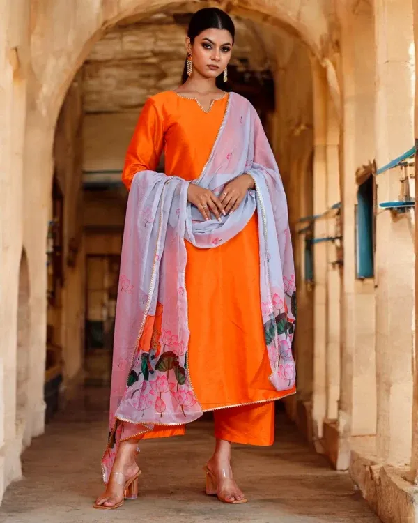 A structured orange dupion suit set paired with a grey Pichwai printed chiffon dupatta from Golden Muslin by Priyanka Rathore, blending heritage artistry with festive elegance.